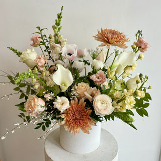 A floral arrangement with a variety of flowers in shades of white, pink, and dusty pink, placed in a white ceramic pot.
