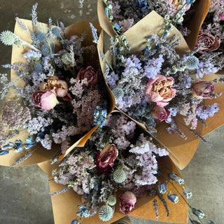 Bouquets of dried flowers in brown paper packaging on a concrete floor.