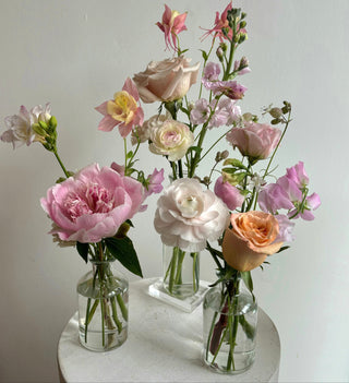 Three clear glass bud vases with various florals arrangement in them
